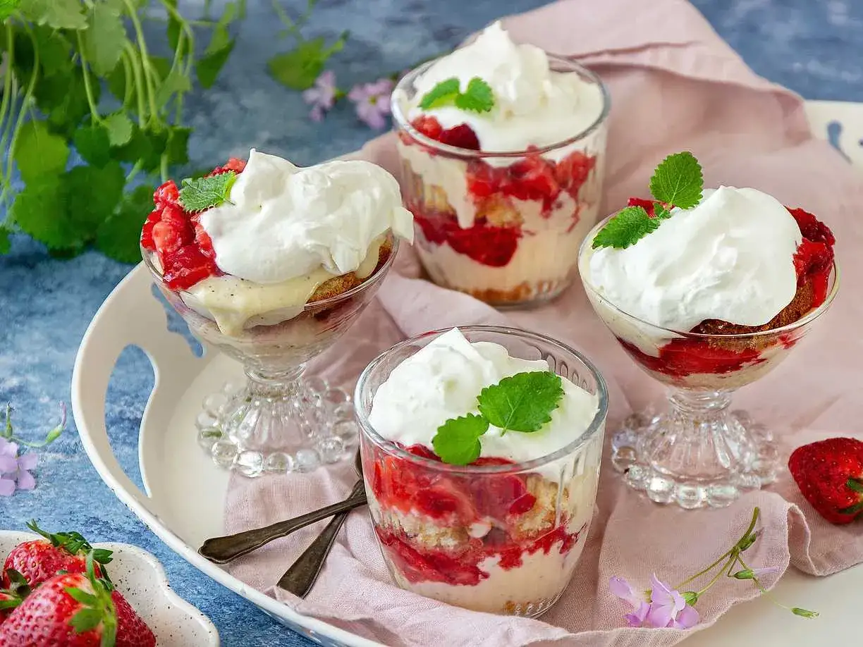 Fyra läckra jordgubbstårtor i glas, toppade med vispgrädde och mynta. Perfekt sommardessert!