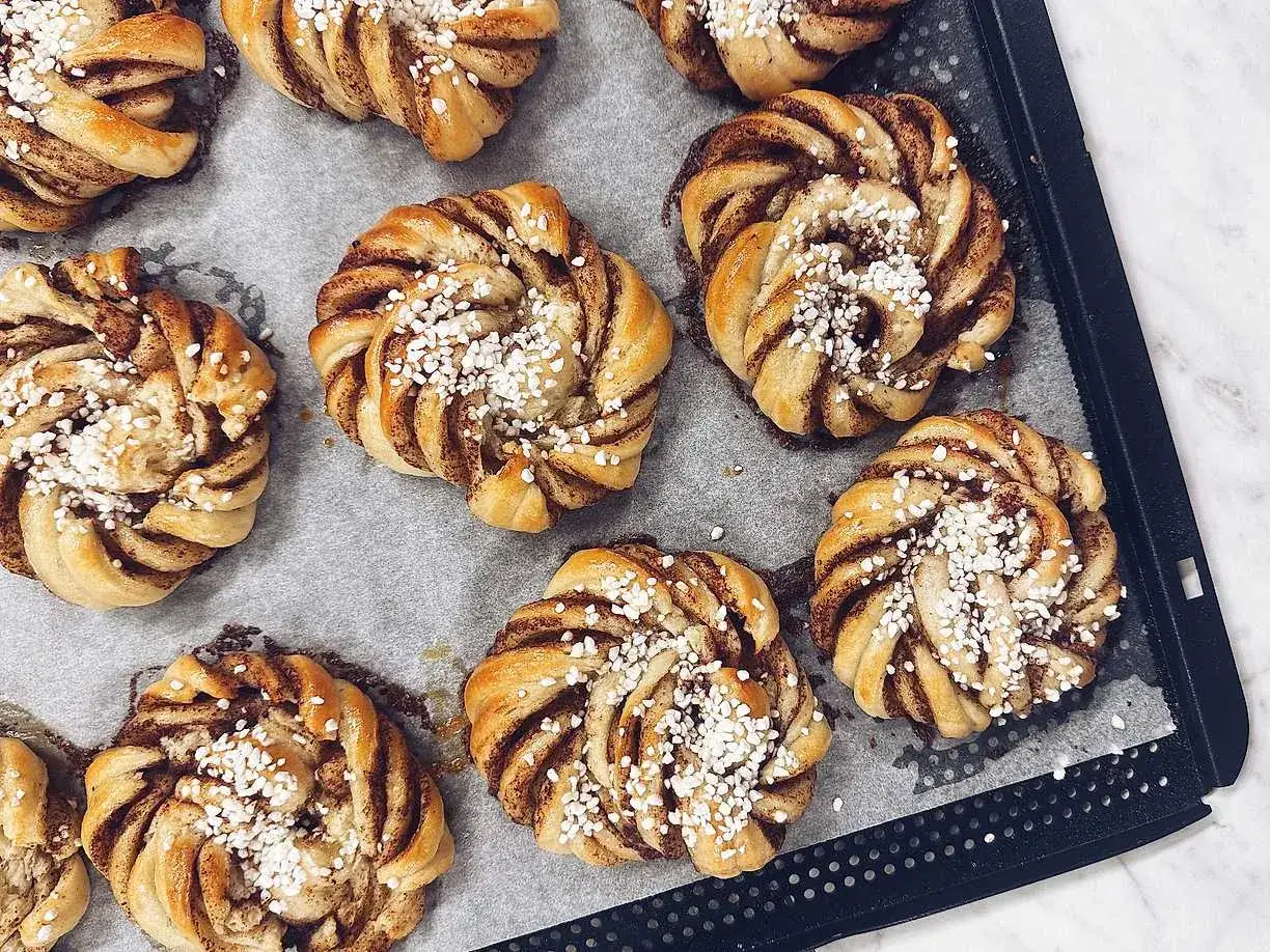 Nybakade kanelbullar med pärlsocker, redo att avnjutas. En härlig kanelbulle längd på bakplåtspapper.