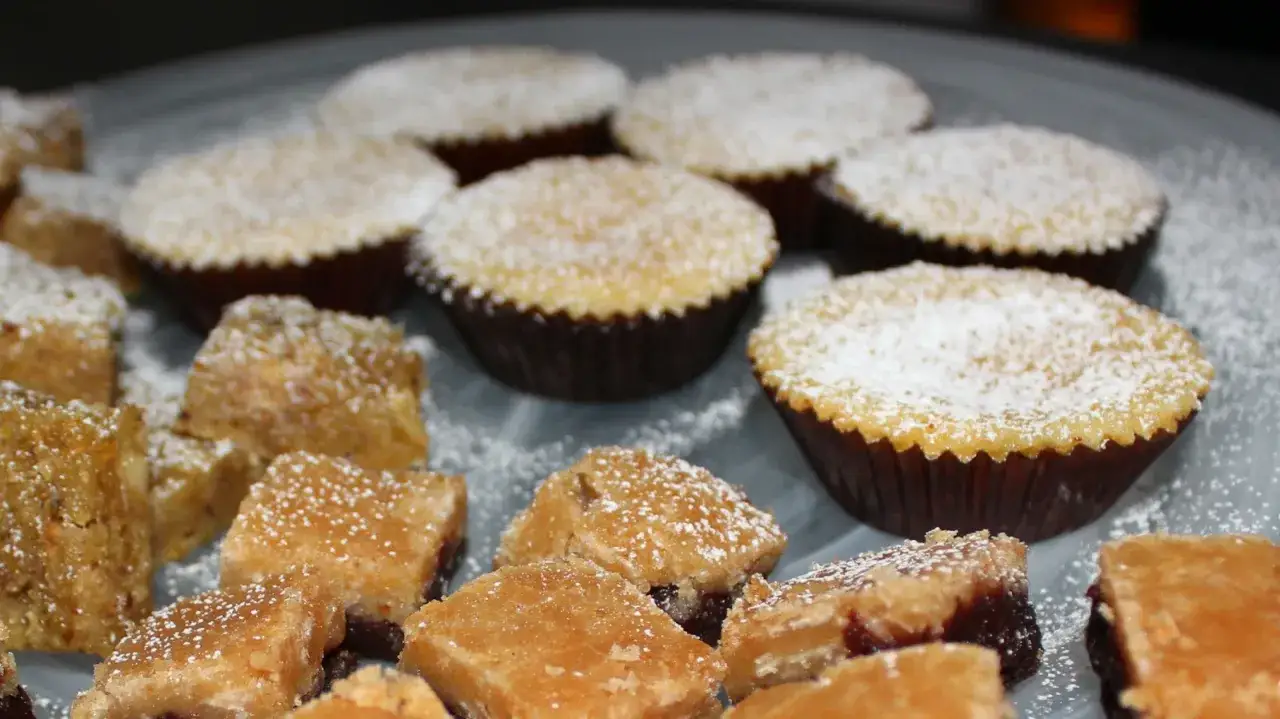 Saffransmuffins med mandelmassa, pudrade med florsocker, ligger p&aring; ett fat tillsammans med fyrkantiga bitar av en annan godsak.