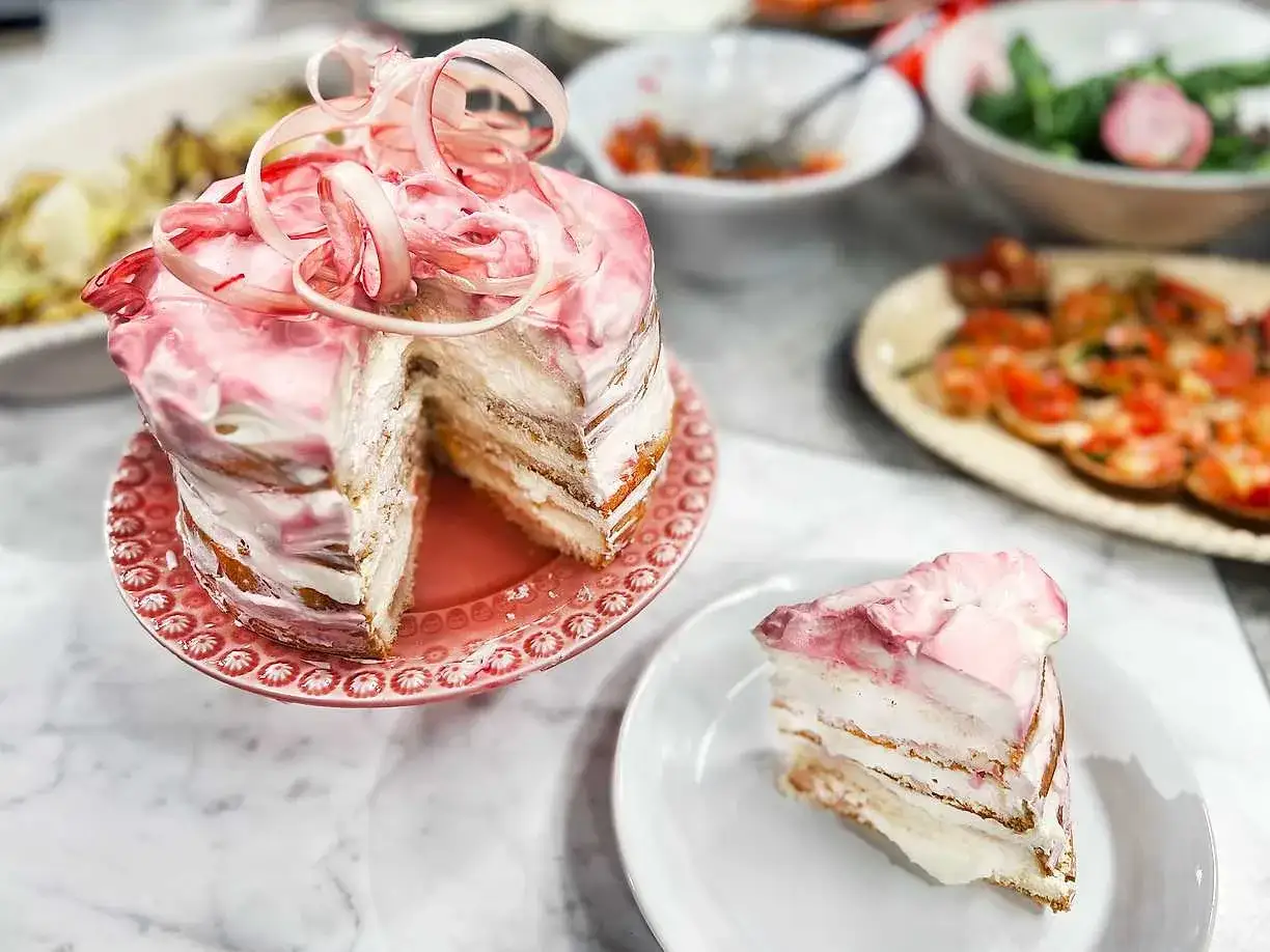 En vacker rabarberkompott tårta med rosa frosting och en skiva upplagd. Perfekt för sommaren!