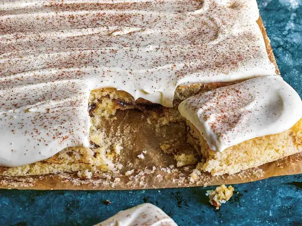 En saftig sockerkaka med krämig glasyr och ett generöst strössel av kanel. En bit saknas, redo att avnjutas.
