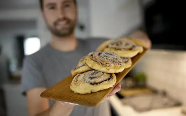 Man håller fram en bricka med nybakade kanelbullar utan ägg, strösslade med socker.